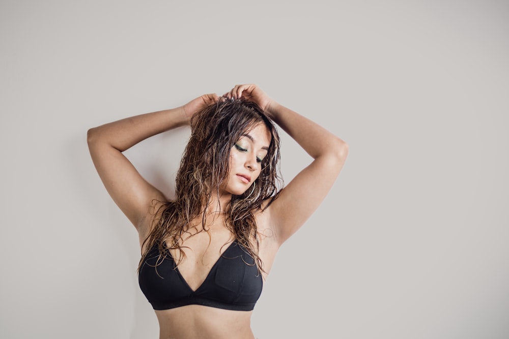 a woman in a black bikini top with her hands on her head