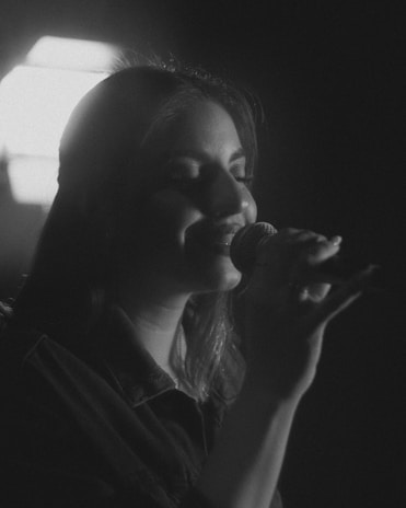 Female singer performing in a minimalist setting with soft black and gold background tones.