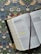 An open Bible lies on a floral patterned surface, with passages highlighted in yellow. The pages show sections with red text, indicating words of significance, and a red ribbon bookmark is placed between the pages. The background features an ornate design with birds, flowers, and leaves.
