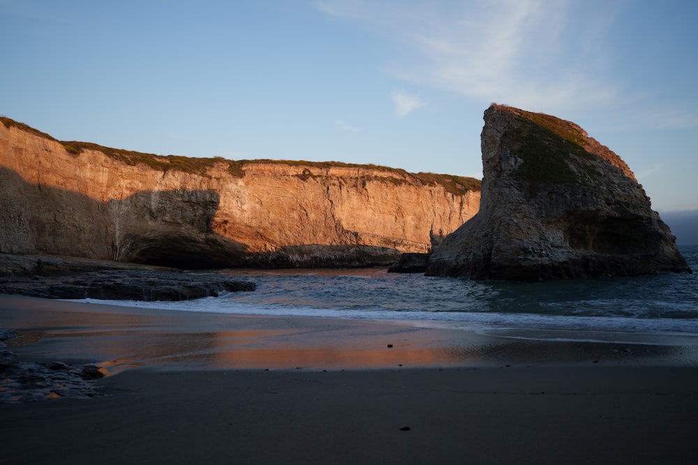 a large rock sticking out of the ocean next to a beach