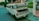 A white van is parked on the side of a street with its hood open, revealing the engine. The van has the word 'RUTA' printed on the front window. It is situated near a residential area with a fence and greenery in the background.