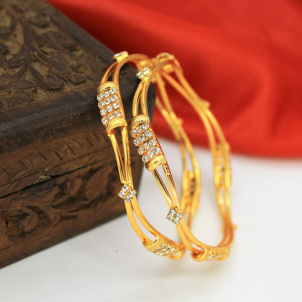 a pair of gold bracelets sitting on top of a wooden box
