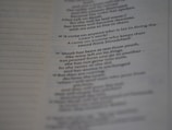 A close-up view of a printed page with text in English. The text appears to be from a religious scripture, specifically verses or passages, with some words in bold.
