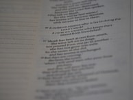A close-up view of a printed page with text in English. The text appears to be from a religious scripture, specifically verses or passages, with some words in bold.