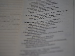A close-up view of a printed page with text in English. The text appears to be from a religious scripture, specifically verses or passages, with some words in bold.