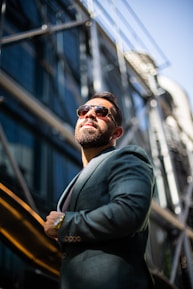 A confident man wearing a perfectly fitted bespoke suit, standing in a sunlit urban street.