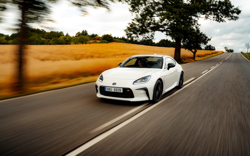 a white sports car driving down a country road