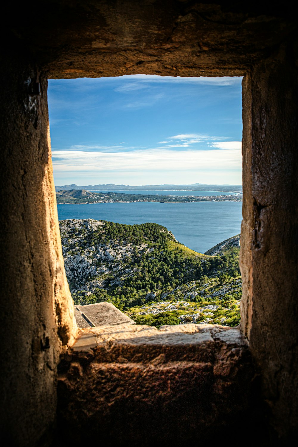 a window in a stone wall with a view of the ocean