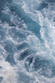 A dynamic pattern of turbulent ocean waves with swirling white foam creating intricate textures and movement.