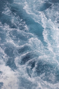 A dynamic pattern of turbulent ocean waves with swirling white foam creating intricate textures and movement.