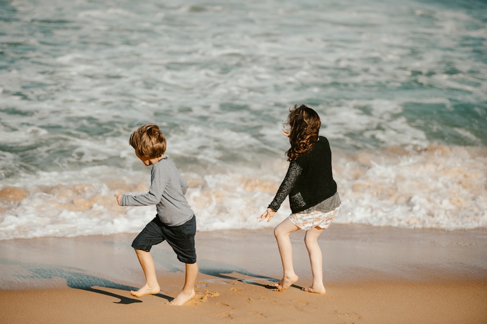 two young children playing on the beach near the ocean