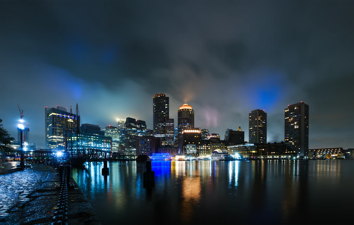 Boston's illuminated downtown skyline at night, its lights reflected in the water