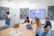 A group of four people engaged in a meeting inside a modern conference room. One person is standing and presenting at a whiteboard filled with a pie chart discussing 'UGC Types', while the others are seated at a table. Laptops and documents are in use, with a large screen displaying an online interface in the background. The room has acoustic wall panels and a neat, modern design.