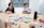 A group of people sitting around a table with various photographs spread out in front of them. One person is holding up a postcard-sized image while others are looking on. The setting is a conference room with a minimalist design and acoustic paneling on the walls. Notepads, pens, and art supplies are scattered across the table.