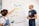 Two individuals are standing next to a whiteboard covered with colorful sticky notes. The woman on the left is pointing at a note while holding a marker, and the man on the right is also holding a marker. The sticky notes have various headings like 'User-Generated Content', 'Engagement', 'Event', and 'Social Wall', each with related subpoints underneath.