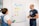 Two people engaged in a discussion in front of a whiteboard. The whiteboard has sticky notes with various categories like 'User-Generated Content' and 'Engagement', each with subcategories noted beneath them. One person holds a marker and an eraser, while the other listens attentively.