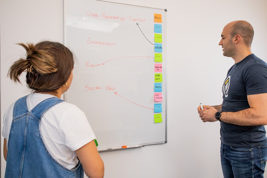 a man and a woman standing in front of a whiteboard, Marketing team discussing marketing terms in front of a white board with post-its
