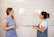 Two people are standing in front of a whiteboard discussing a topic titled 'How to Set Up a Social Wall'. The whiteboard outlines steps: Sign up, Add Sources, Customize, and Share. One person is holding a marker, and both are engaged in conversation, likely explaining the steps.