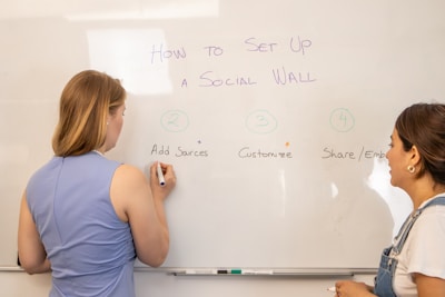 two women are writing on a white board