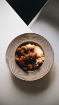 A plate of creamy mashed potatoes topped with a savory, vegetable-based stew. The dish is placed on a textured, neutral-colored plate. The lighting is soft, creating a cozy and inviting atmosphere.