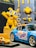 A brightly colored display featuring a yellow cartoon character and various toy cars. The character has large eyes and is raising one arm, surrounded by some toy tools attached to a pegboard. In the foreground, there are two model cars, one larger blue sports car with colorful graphics and a smaller yellow car.
