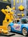 A brightly colored display featuring a yellow cartoon character and various toy cars. The character has large eyes and is raising one arm, surrounded by some toy tools attached to a pegboard. In the foreground, there are two model cars, one larger blue sports car with colorful graphics and a smaller yellow car.