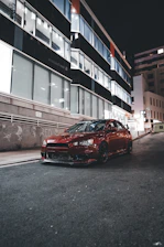 A sleek black sports car gleaming under city lights with a subtle red and blue glow reflecting off its polished surface.