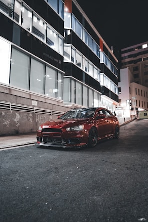 Sleek red sports car gleaming under city lights at dusk.