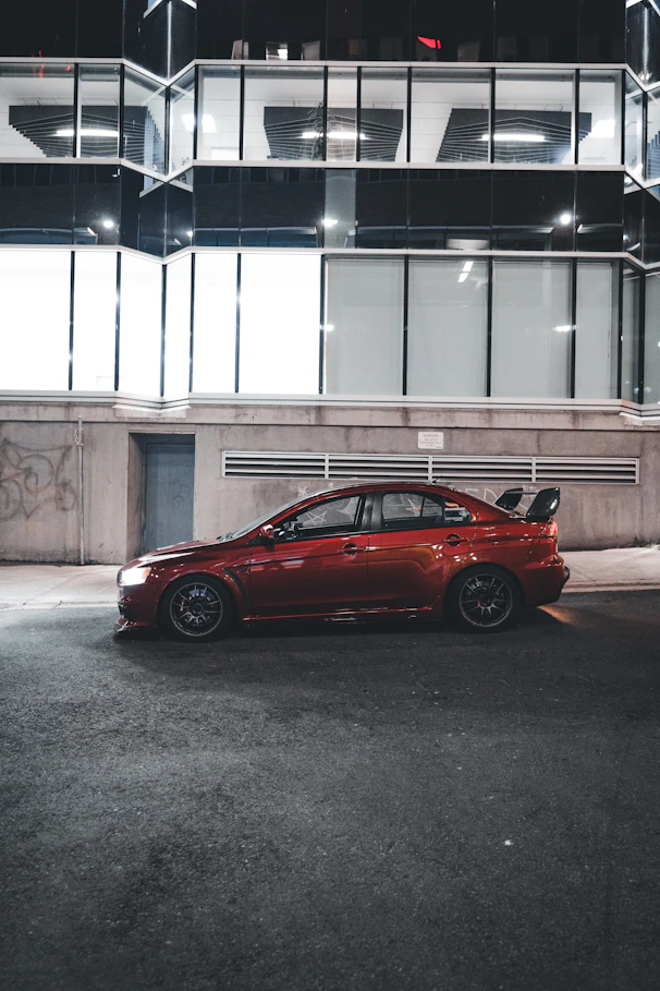 A sleek red sedan parked on a city street at sunset, highlighting its shiny exterior.