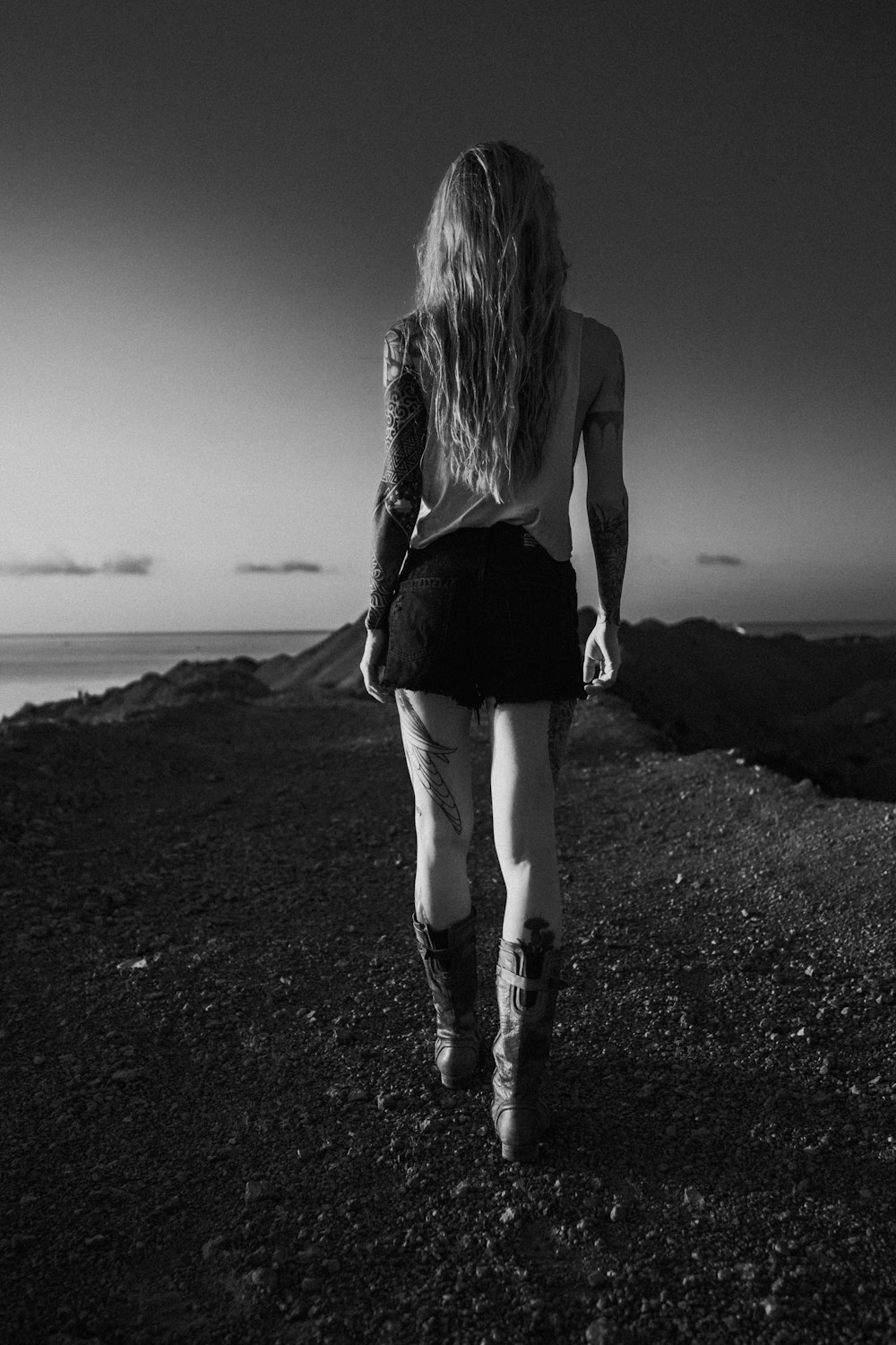 a woman walking down a dirt road next to the ocean