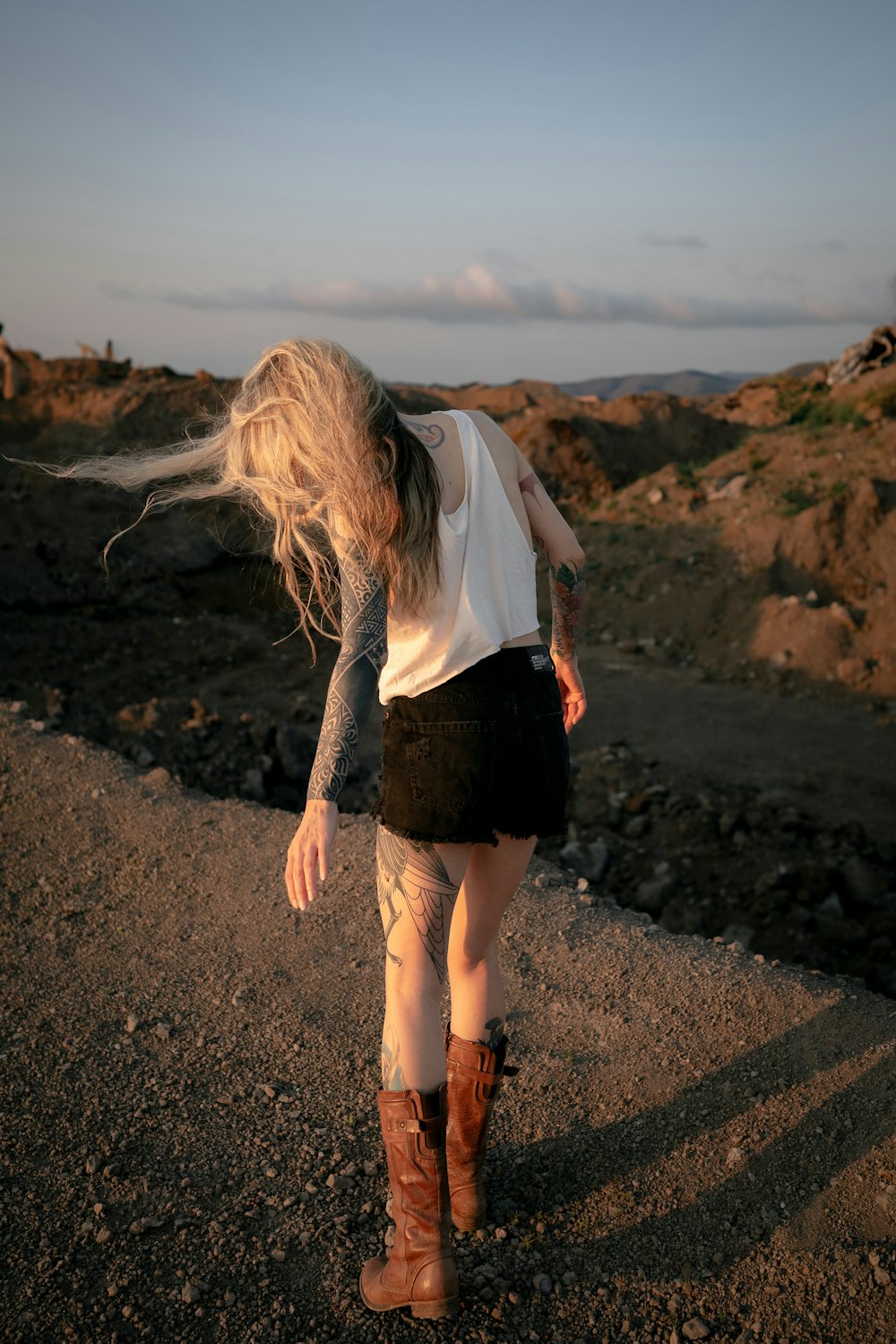 a woman with long hair walking on a dirt road