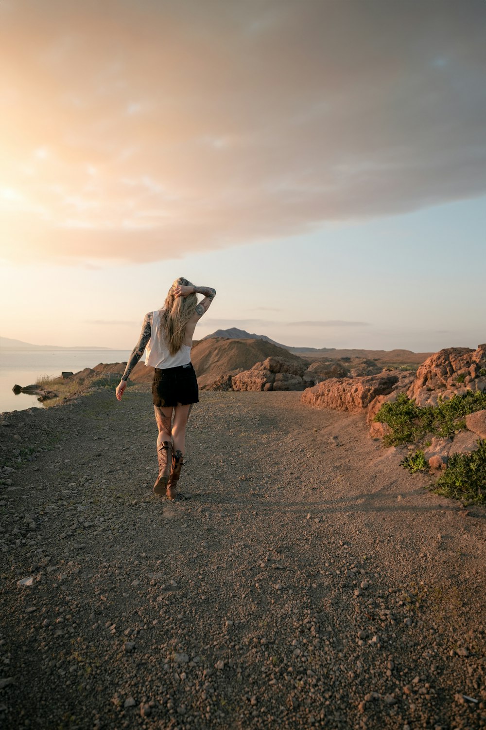a woman walking down a dirt road next to the ocean