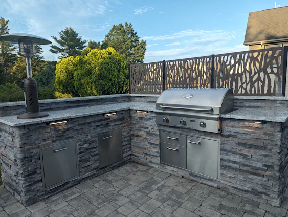 A sleek stainless steel outdoor kitchen island with a built-in grill set up in a sunny backyard.