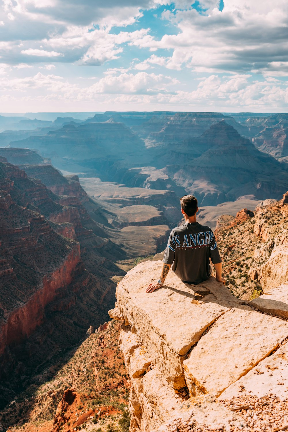 a man sitting on top of a cliff overlooking a canyon