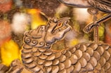 A detailed artistic depiction of a dragon's head and upper body with intricate scales and swirling patterns. The dragon has an open mouth and elongated snout. In the foreground, there is a bird's claw resting on some part of the dragon's body. The background consists of blurred, colorful bokeh lights in shades of yellow, orange, and white, giving the piece a dynamic and elegant appearance.