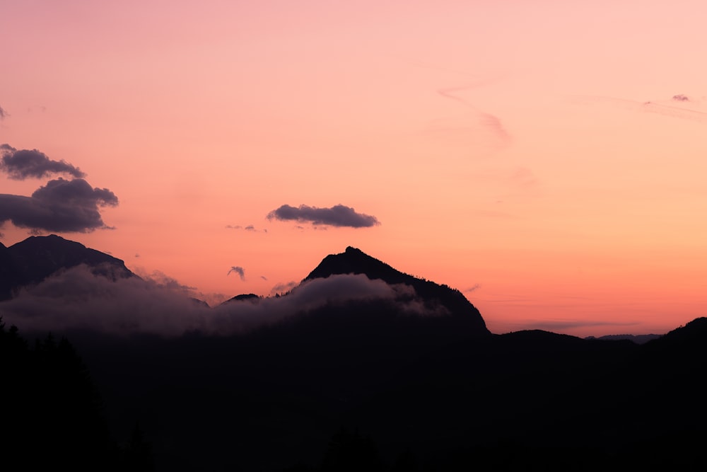 a pink sky with clouds and mountains in the background