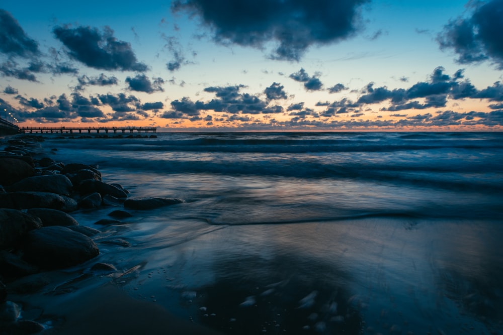 the sun is setting over the ocean with a pier in the distance