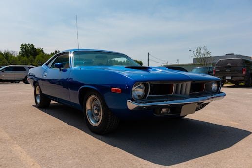 A gleaming red 1969 muscle car parked under a clear blue sky, surrounded by vintage automotive memorabilia.