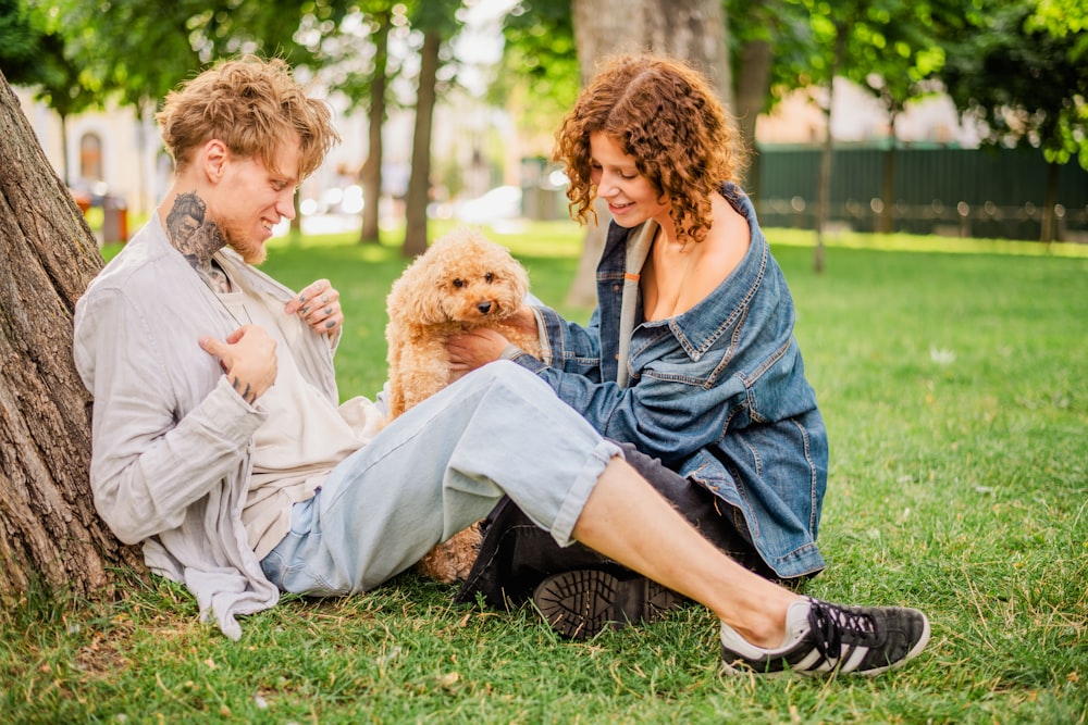 a man and woman sitting next to a tree with a dog