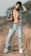 A man with a casual pose stands in a field, wearing ripped jeans and an open denim jacket, highlighting a relaxed and rugged style.