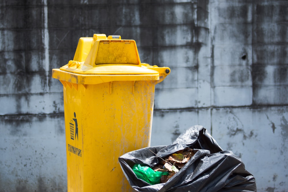 a yellow fire hydrant next to a trash bag