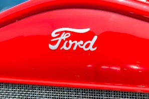A red car grille showcasing the Ford logo in white, with a metallic mesh below it.