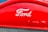 A red car grille showcasing the Ford logo in white, with a metallic mesh below it.