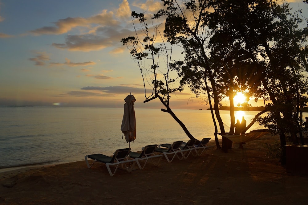 the sun is setting over a beach with lounge chairs