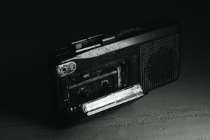 An old-fashioned tape recorder surrounded by scattered evidence photos and a glass of whiskey.