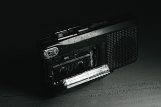 An old-fashioned tape recorder surrounded by scattered evidence photos and a glass of whiskey.