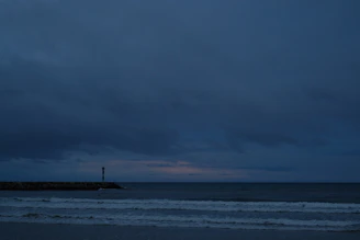A calm sea horizon under a navy sky with golden beams of lighthouse light cutting through.