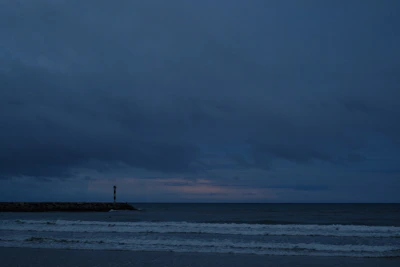 A calm sea horizon under a navy sky with golden beams of lighthouse light cutting through.