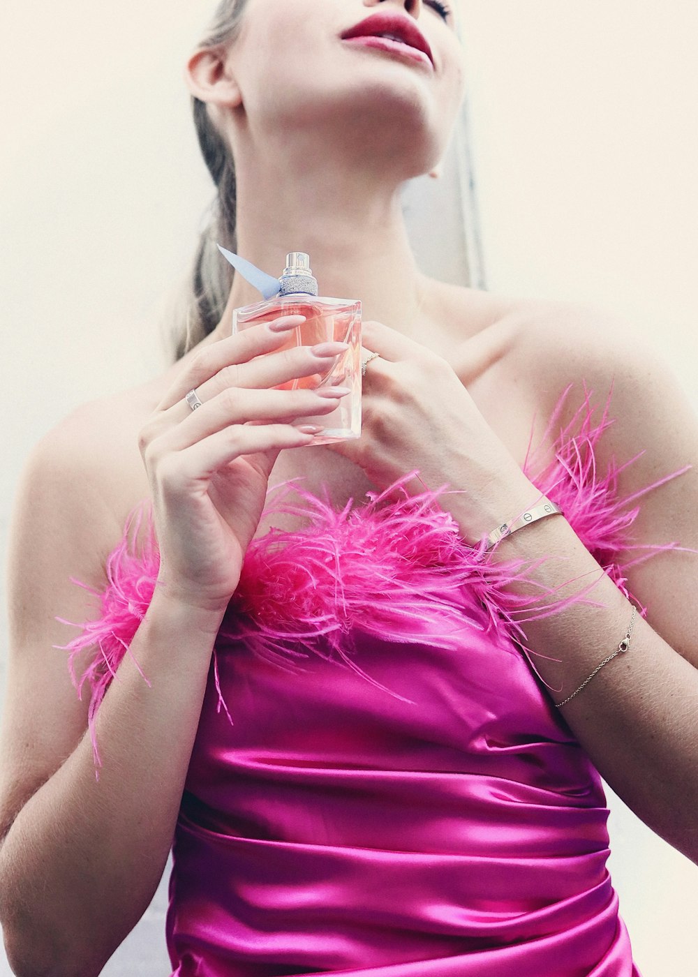 a woman in a pink dress holding a bottle of perfume