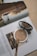 A makeup compact and brush rest on the pages of an open magazine. The magazine features an image of a woman with wavy hair looking back over her shoulder at the camera. Text is visible on the pages, and the overall setting creates a sense of everyday beauty and style.